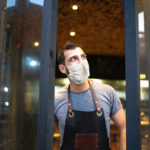 Small business owner closing front door with face mask