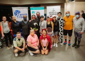 Picture of people standing in front of banners for CMHA, Tennis Troupe and Runers & Rackets, wearing costumes and smiling